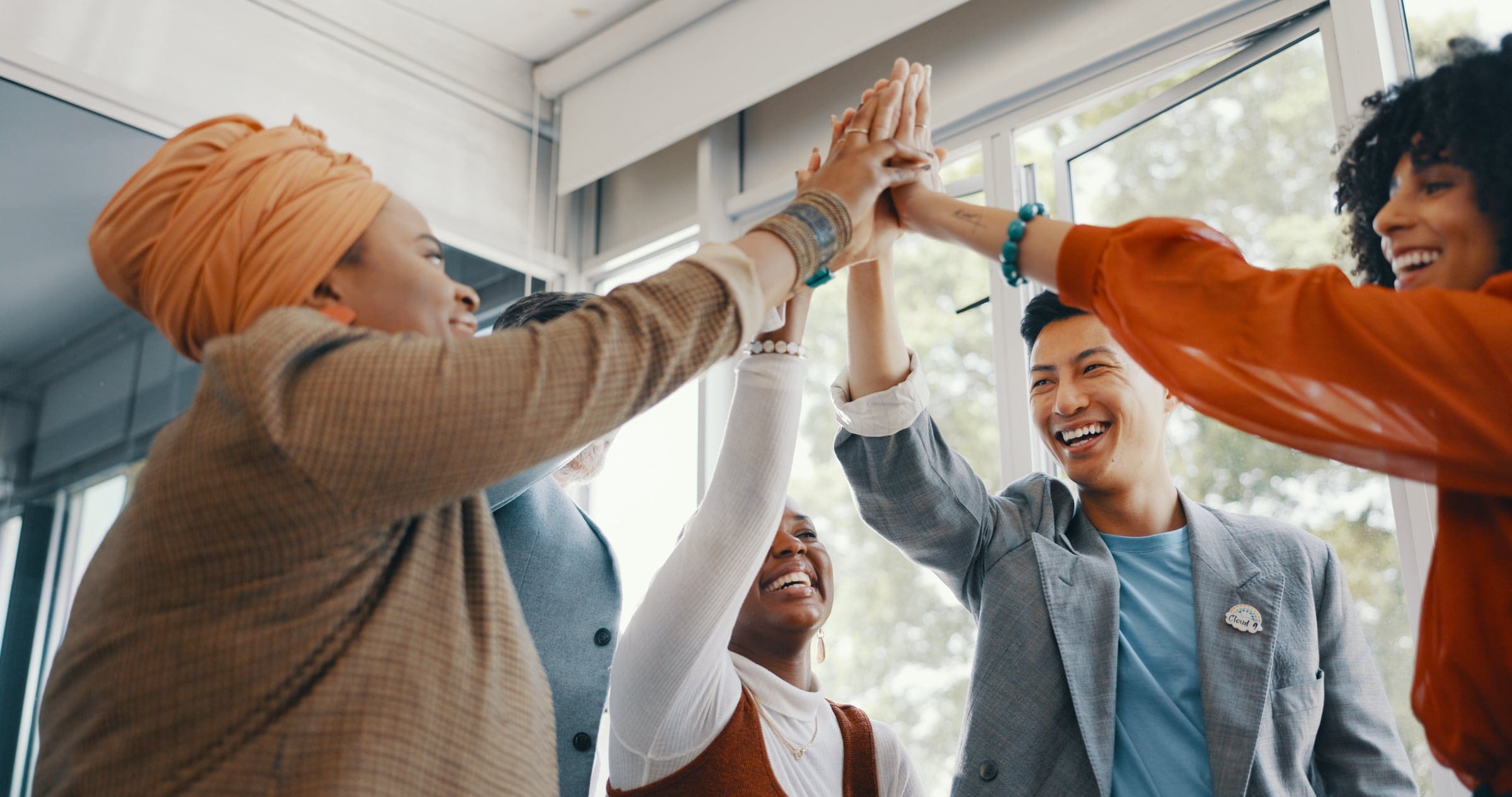 Individuals from varying races and ethnicities smiling while raising their arms in the air and touching hands.